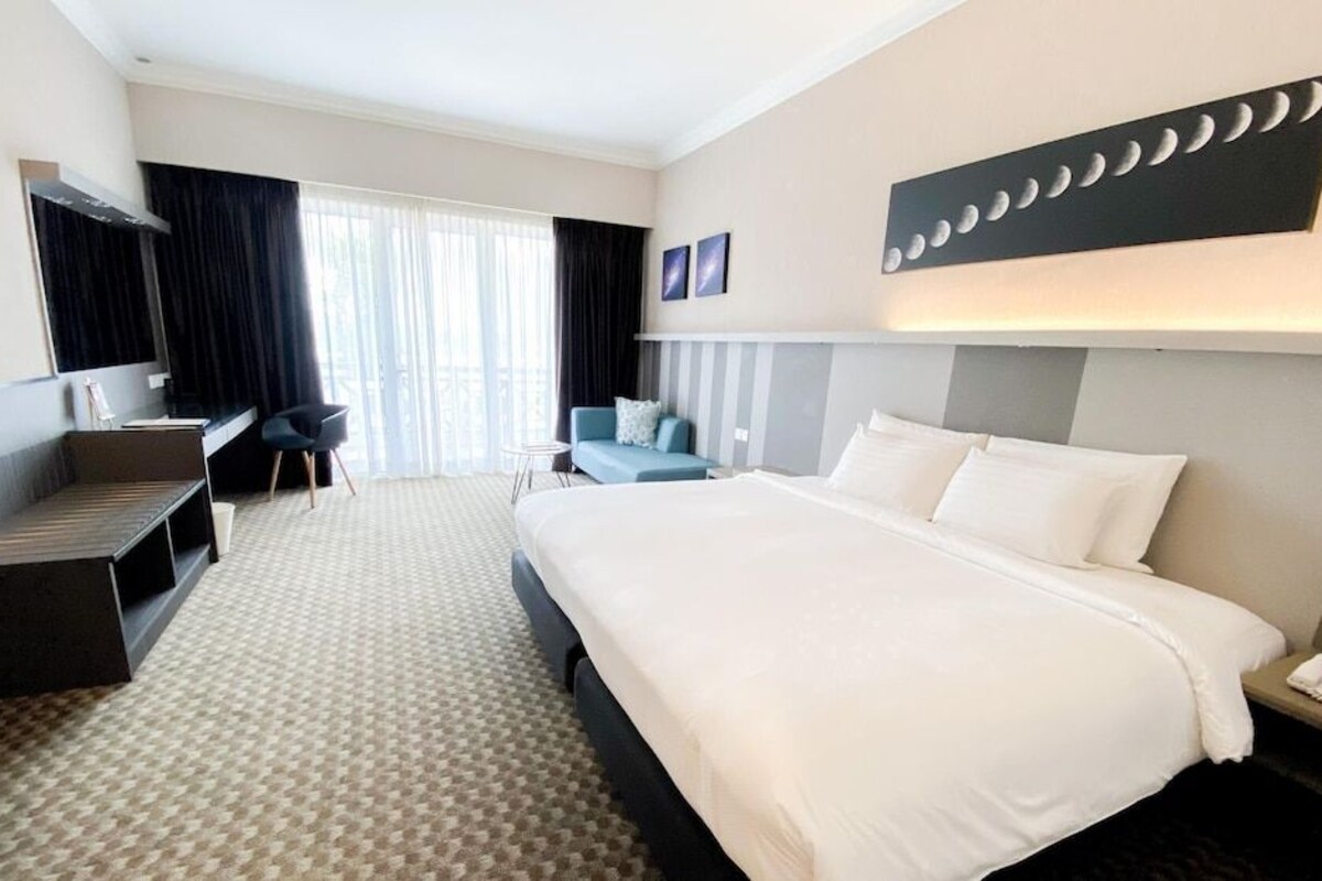 A hotel room with a large bed, a desk, a chair, and a sofa.
