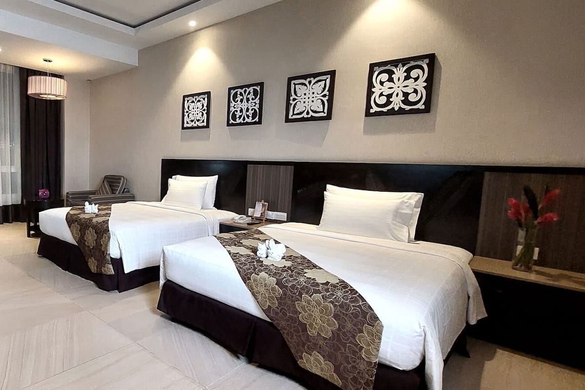 A hotel room with two beds, a desk, a chair, and a large window with curtains.