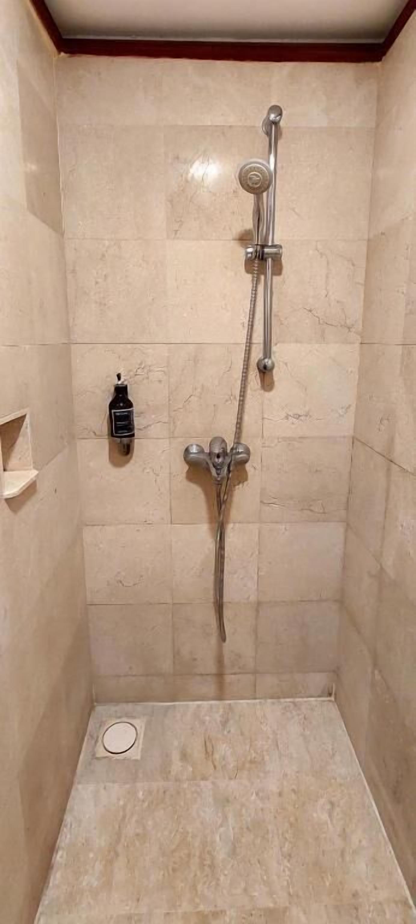 Un pequeño baño revestido de azulejos con ducha de mano y grifo empotrado.