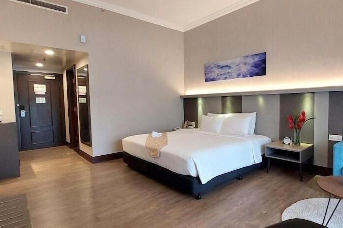 A hotel room with a bed, a nightstand, a blue armchair, a small table, and artwork on the walls.