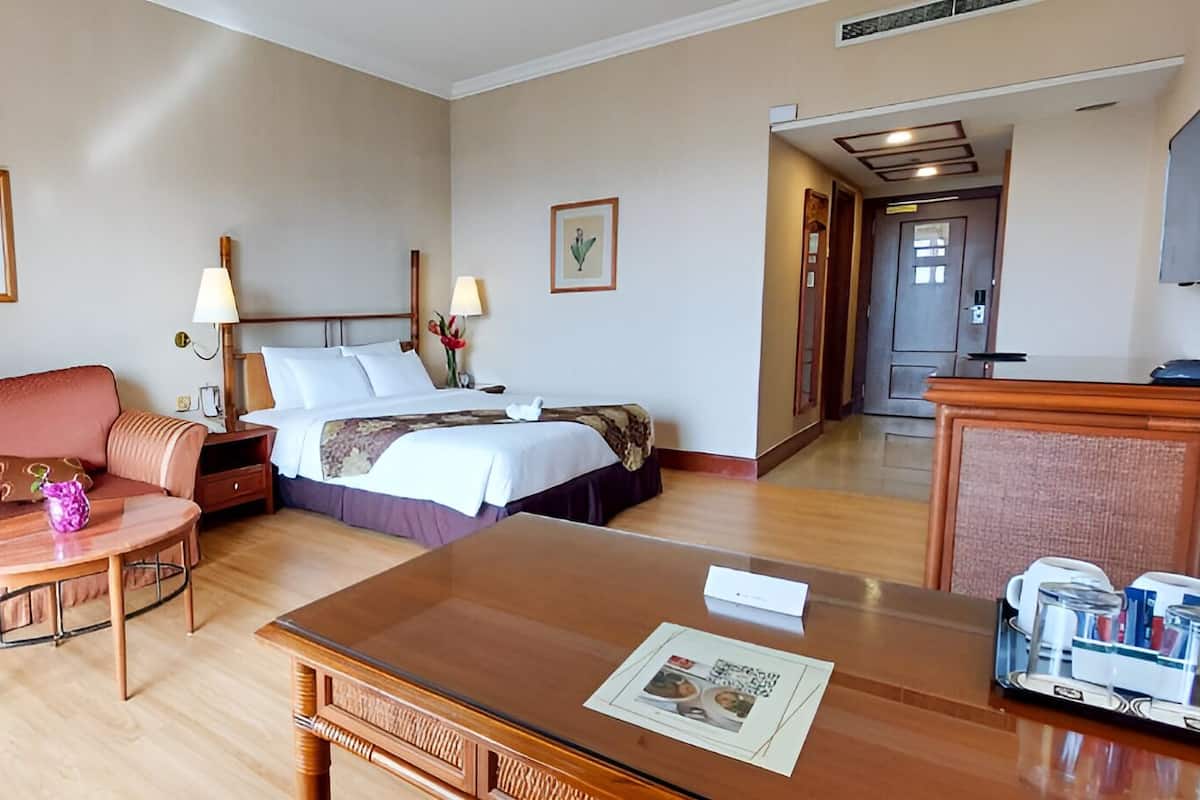 A hotel room with a sofa, a bed, a desk, and a lamp.