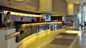 Una moderna zona de recepción de hotel con un mostrador curvo, grandes lámparas cilíndricas y suelo de mármol.