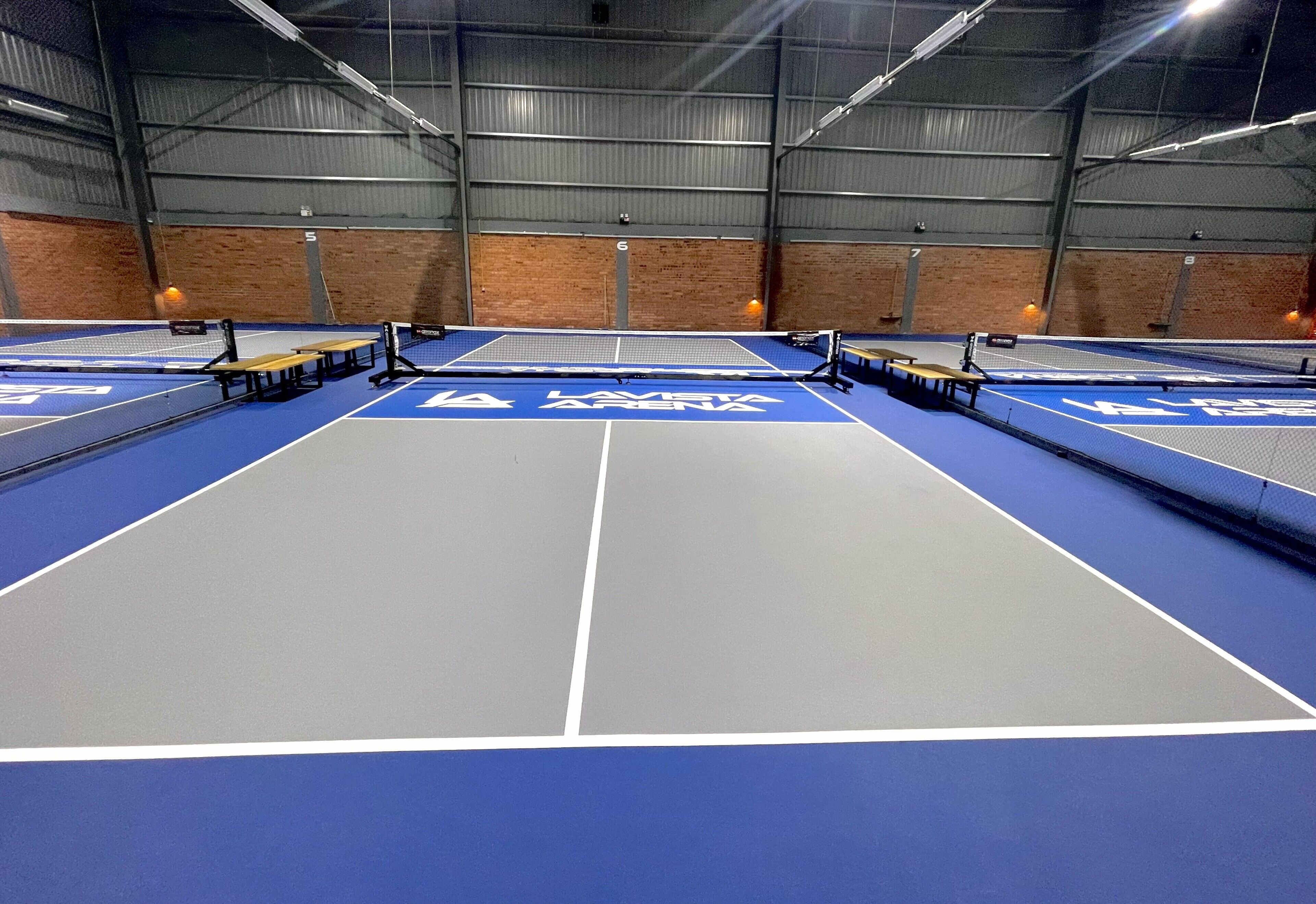 Instalación de tenis en interiores con varias canchas, vigas metálicas y paredes de ladrillo.
