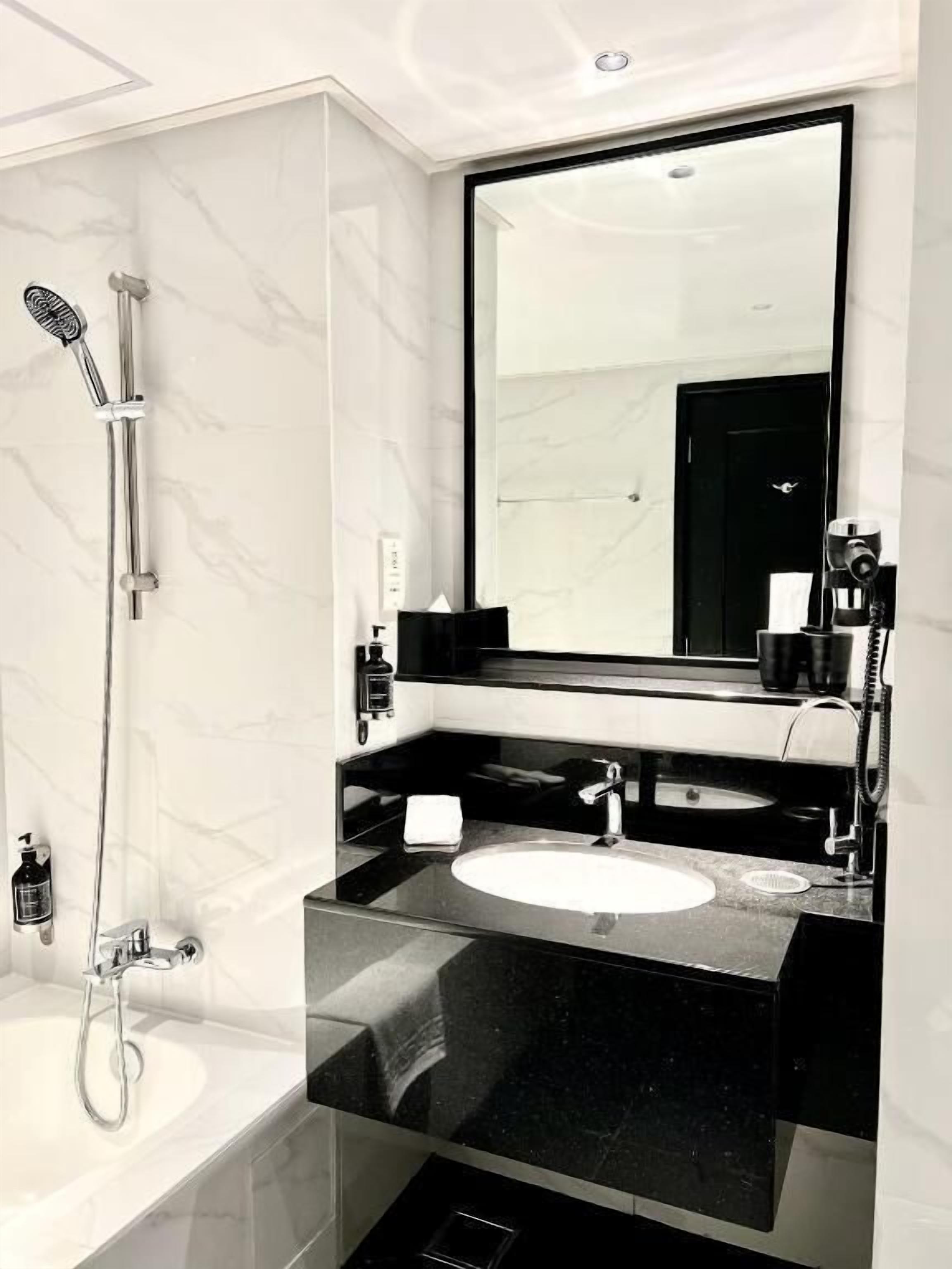 A modern bathroom with a large mirror, a bathtub, and a vanity with a sink.