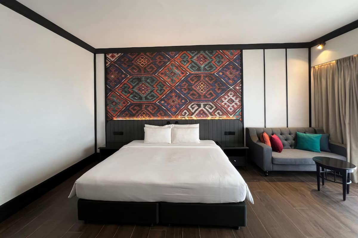 A modern hotel room with a large bed, a sofa, and a patterned wall hanging.