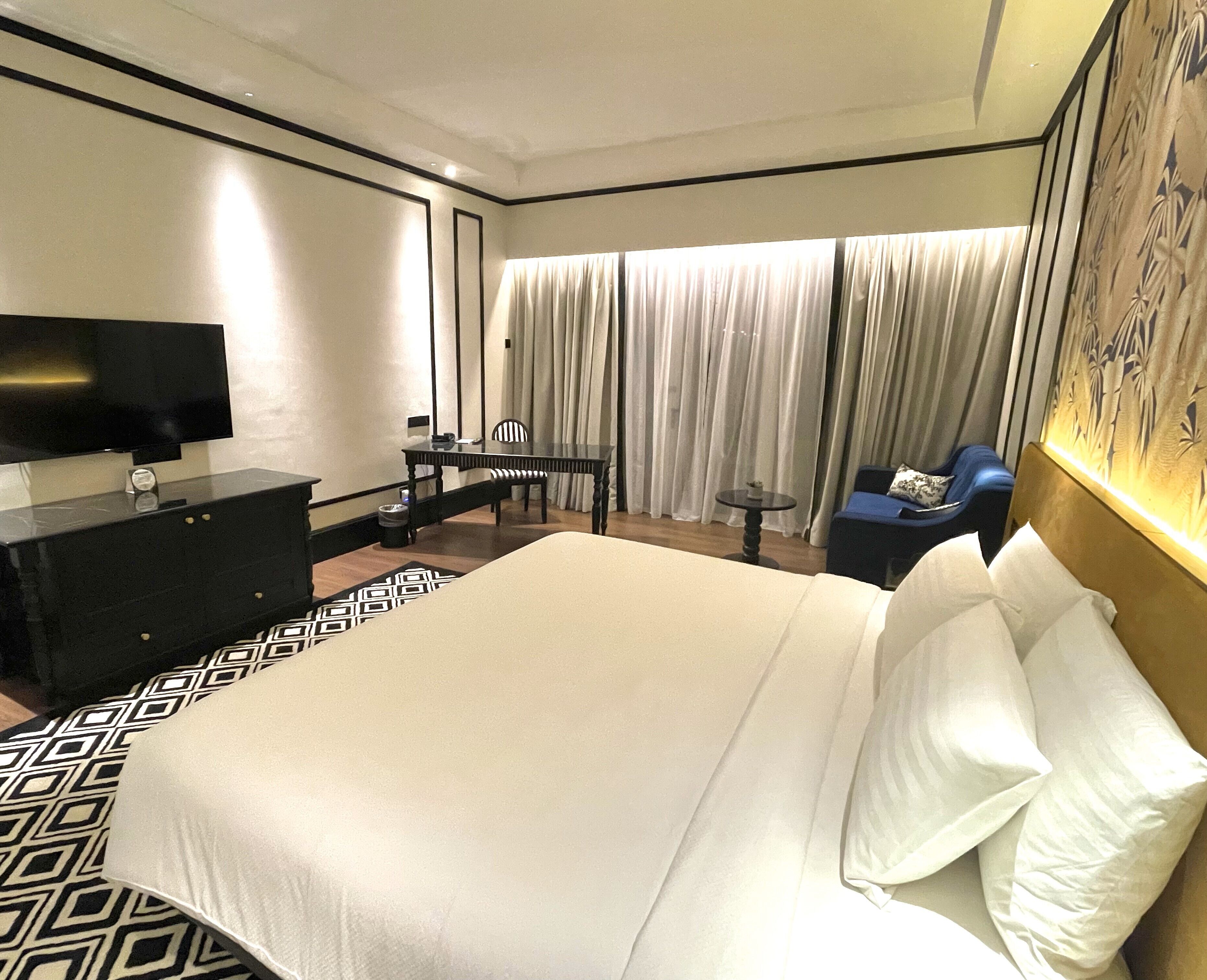 A hotel room with a large bed, a desk with a chair, a television, and a window with curtains.
