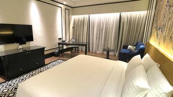 A hotel room with a large bed, a desk with a chair, a television, and a window with curtains.