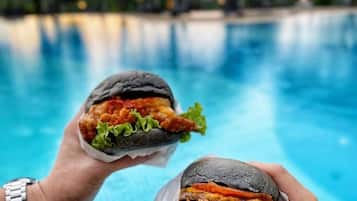 Dos manos sosteniendo hamburguesas sobre una piscina.