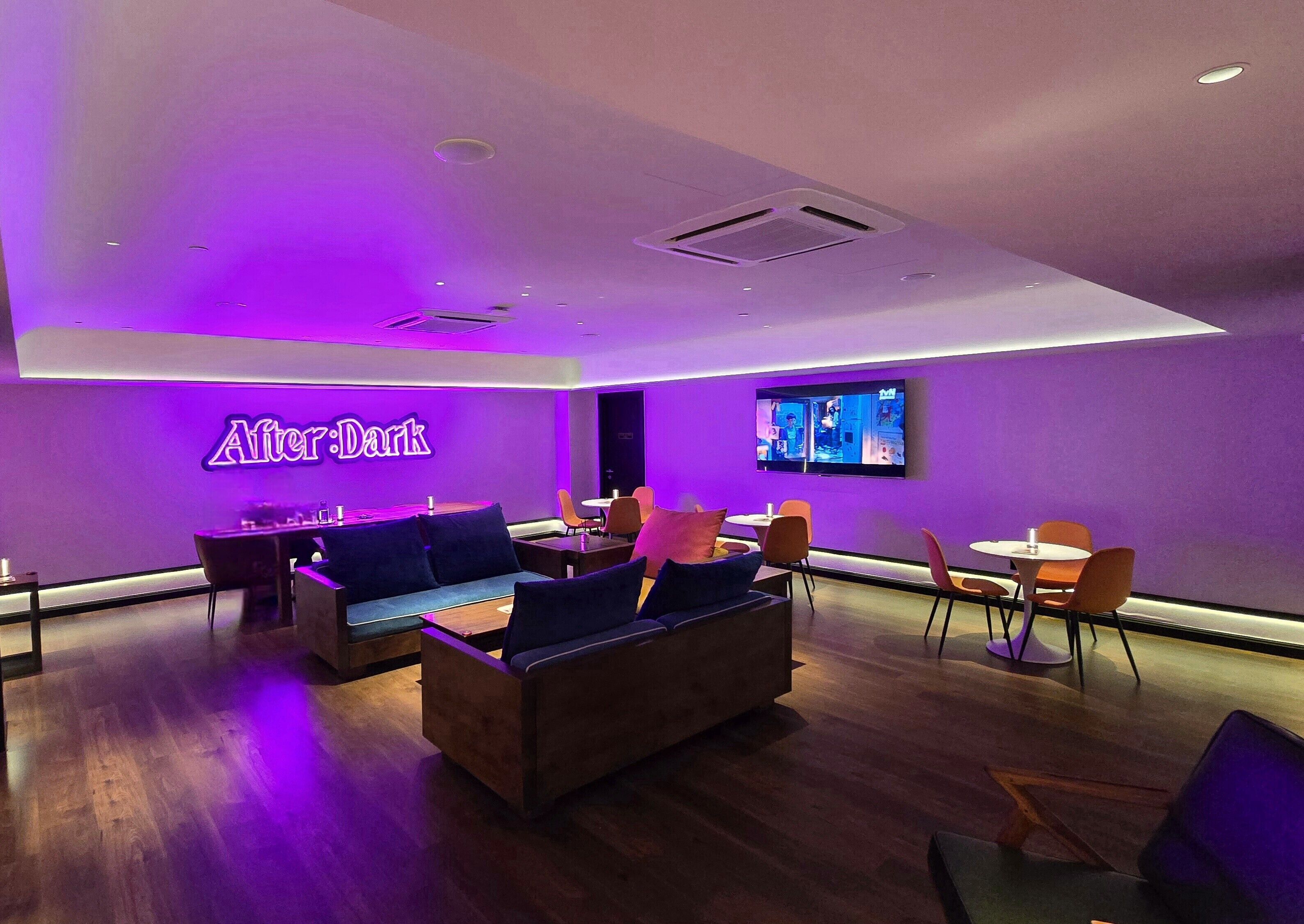 A modern lounge area with a neon sign, seating arrangements, and a television.