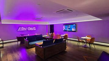 A modern lounge area with a neon sign, seating arrangements, and a television.