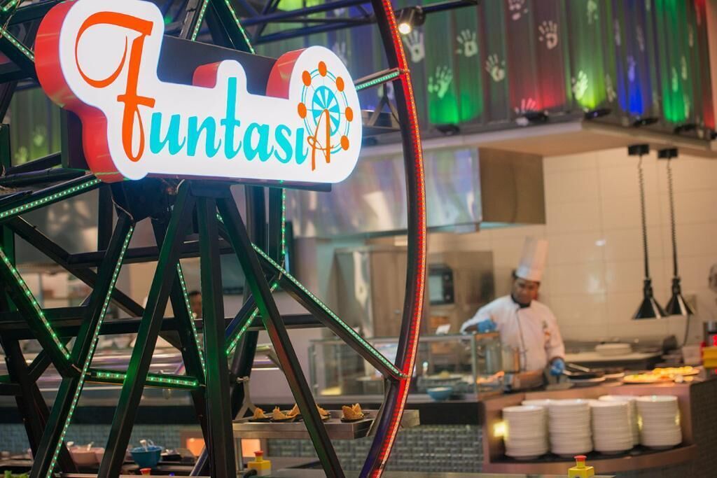 A Ferris wheel with a sign that reads "Funtasi" and a chef preparing food in the background.