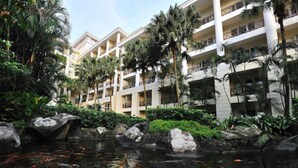 Un hotel con varios balcones, un estanque de carpas y jardinería tropical.