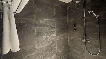 A modern shower area with dark marble tiles, a handheld showerhead, and a towel rack with white towels.