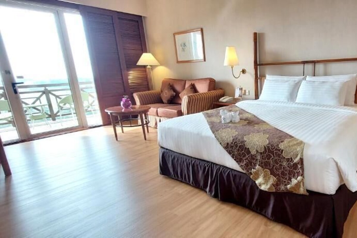 A hotel room with a large bed, a sofa, a small table, and a nightstand with a lamp.