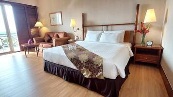 A hotel room with a large bed, a sofa, a small table, and a nightstand with a lamp.