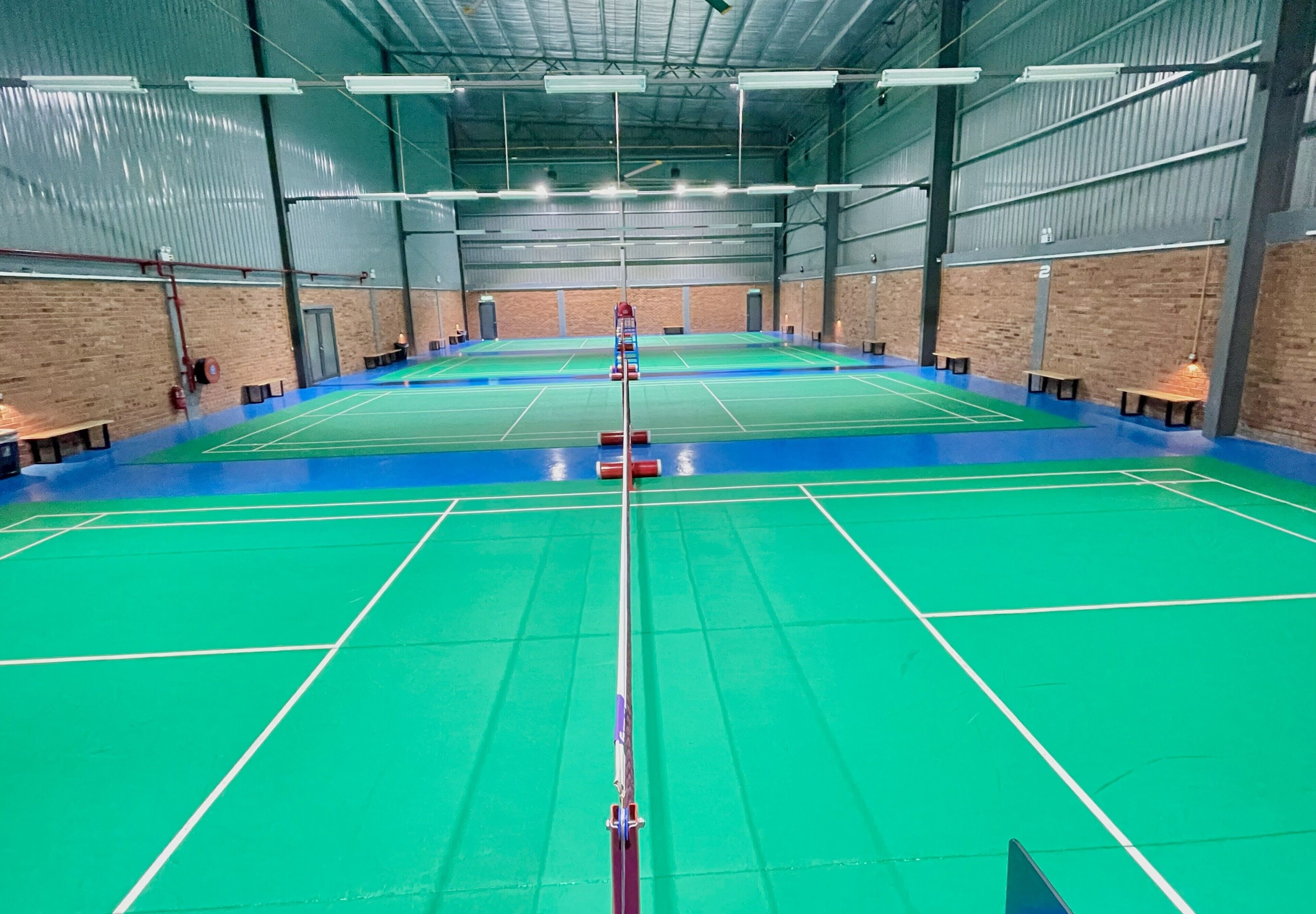 An indoor badminton court with a net, benches, and a high ceiling with lighting fixtures.