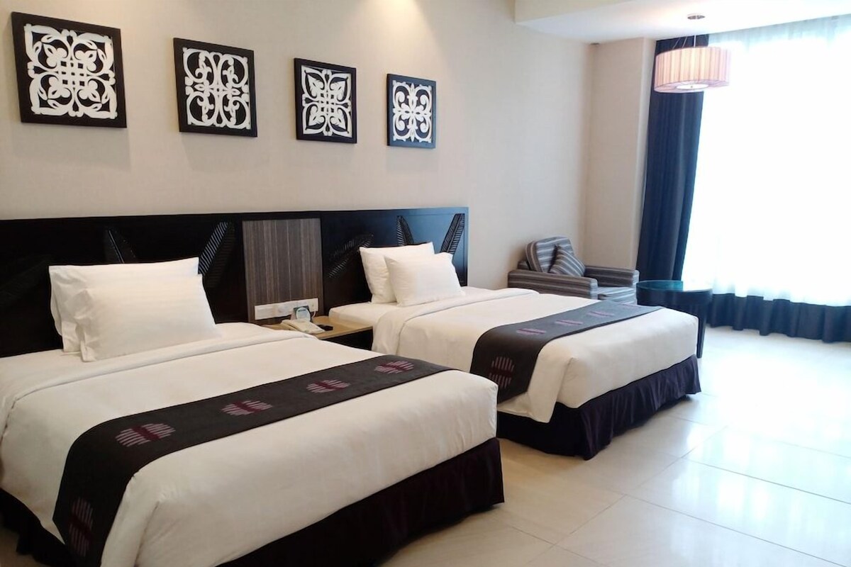 A hotel room with two beds, a nightstand, a lamp, and artwork on the wall.