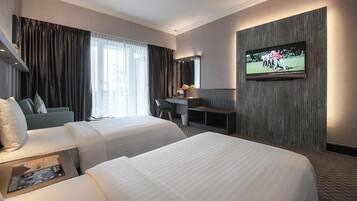 A hotel room with two beds, a desk, a TV, and a large window with curtains.