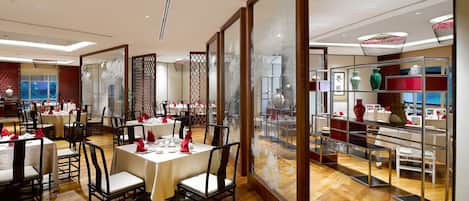 A restaurant with multiple tables set for dining, wooden flooring, and a view of the interior through a glass partition.