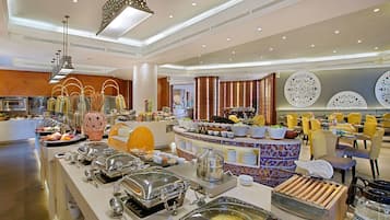 Zona de bufé con diferentes estaciones de comida, incluyendo una parrilla caliente y una variedad de platos exhibidos en un mostrador.