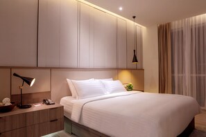 A modern hotel room with a large bed, a bedside table with a lamp, a phone, and a bowl of fruit.