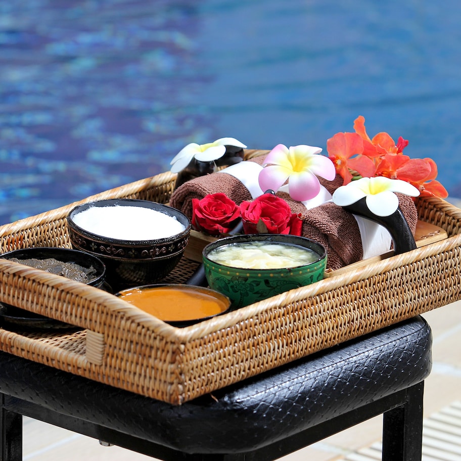 A spa treatment set with towels, flowers, and bath products by a pool.