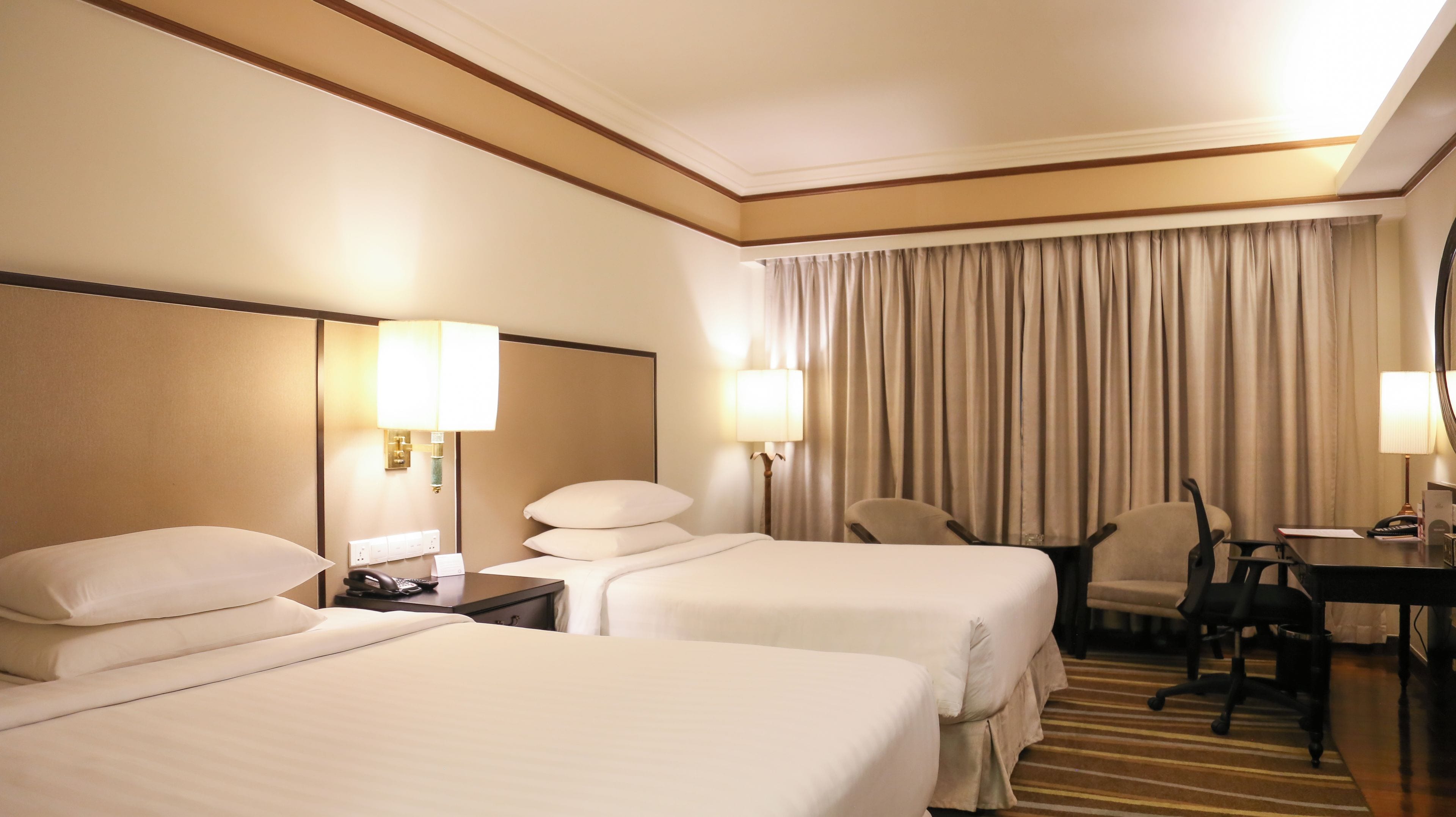 A hotel room with two beds, a desk, a chair, and a large window with curtains.