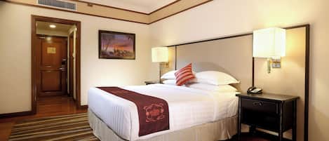 Una habitación de hotel con una cama grande, dos mesitas de noche con lámparas, un cuadro en la pared y una puerta que da a otra habitación.