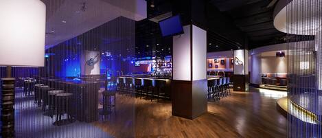 A modern bar area with wooden flooring, bar stools, and a seating area with round tables.