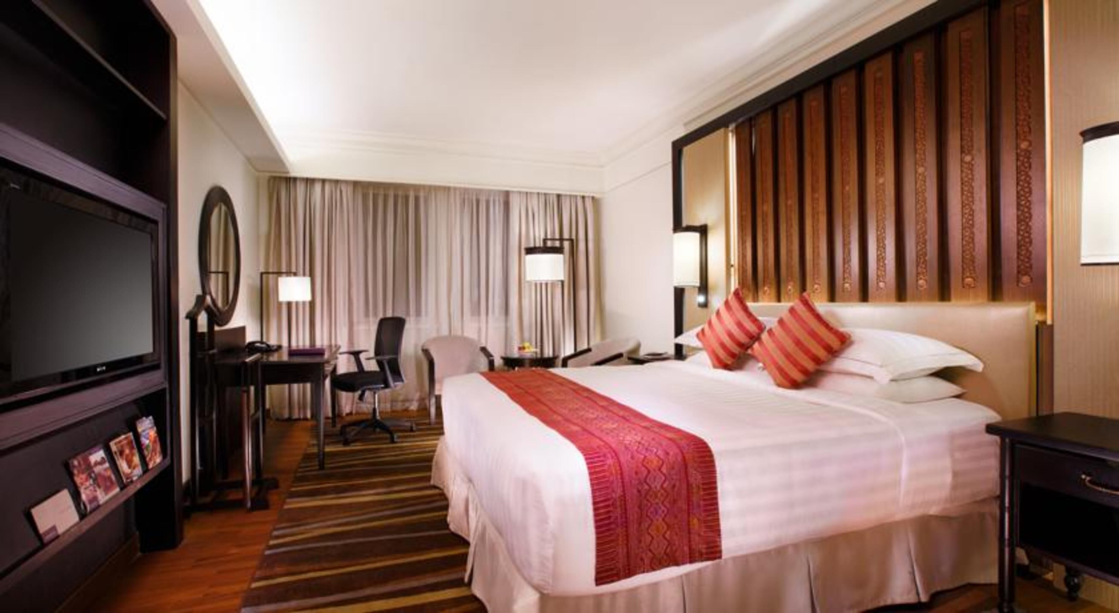 A hotel room with a large bed, a desk with a chair, a television, and a wooden headboard.
