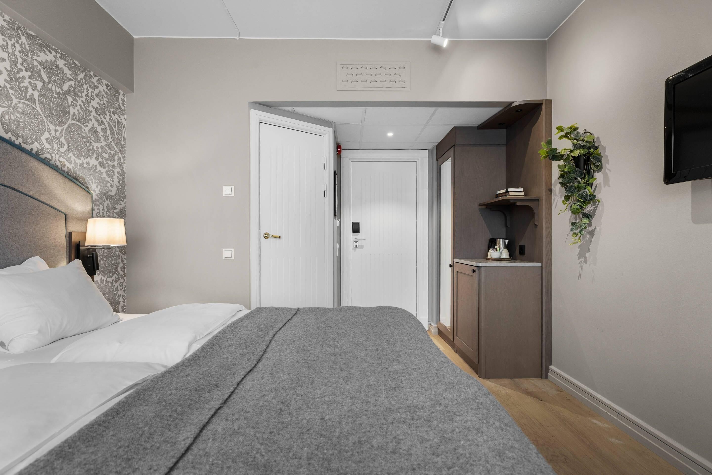 Une chambre d’hôtel équipée d’un lit, d’une lampe de chevet, d’une armoire et d’un téléviseur.