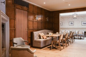 A room with a wooden panel wall, a sofa, a dining table with chairs, and a fireplace. - Home Hotel Bastion (Oslo)