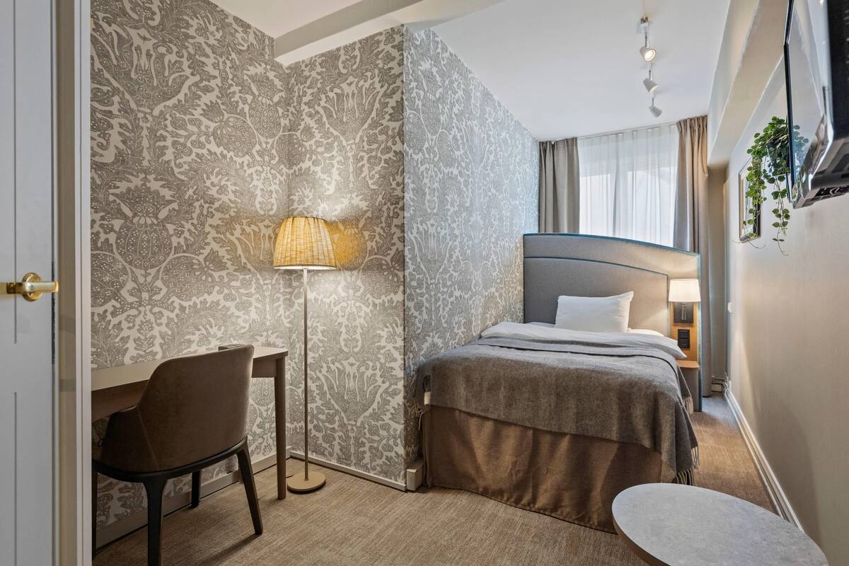 Una habitación de hotel con una cama, un escritorio, una silla, una lámpara y una mesita.