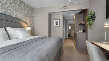 Una camera d'albergo moderna con un letto grande, lampade sui comodini, una scrivania con sedia, un angolo cottura e una pianta decorativa.