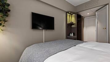 A bedroom with a bed, a flat-screen TV mounted on the wall, a plant, and a door.