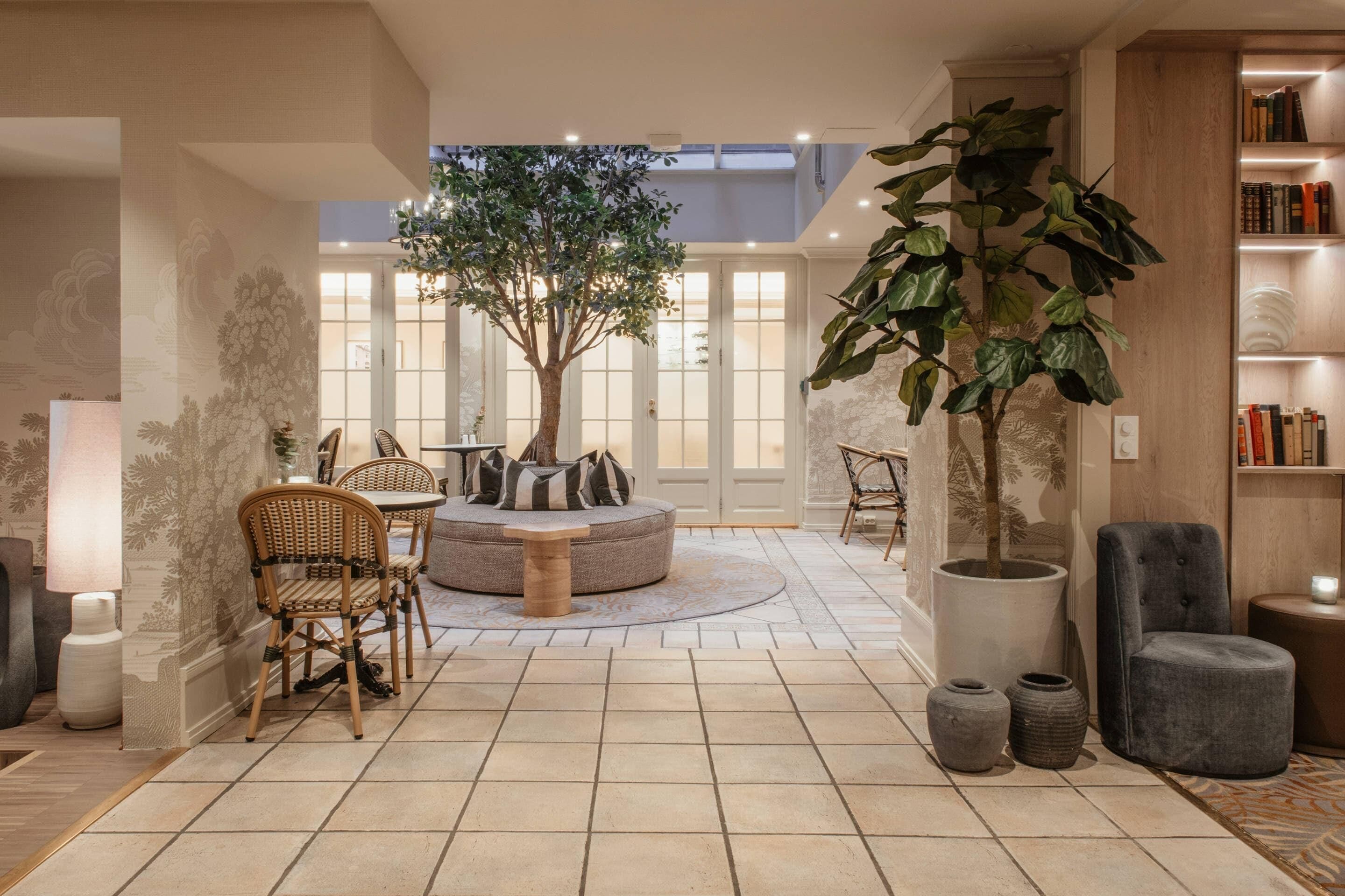 Amplia sala de estar con un árbol grande, asientos redondos y una estantería.