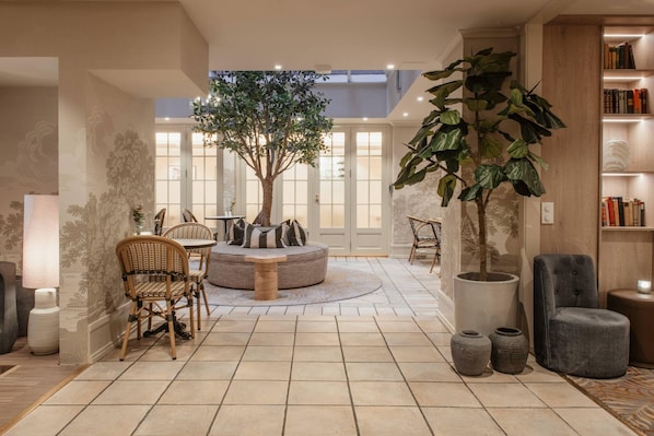 Amplia sala de estar con un árbol grande, asientos redondos y una estantería.