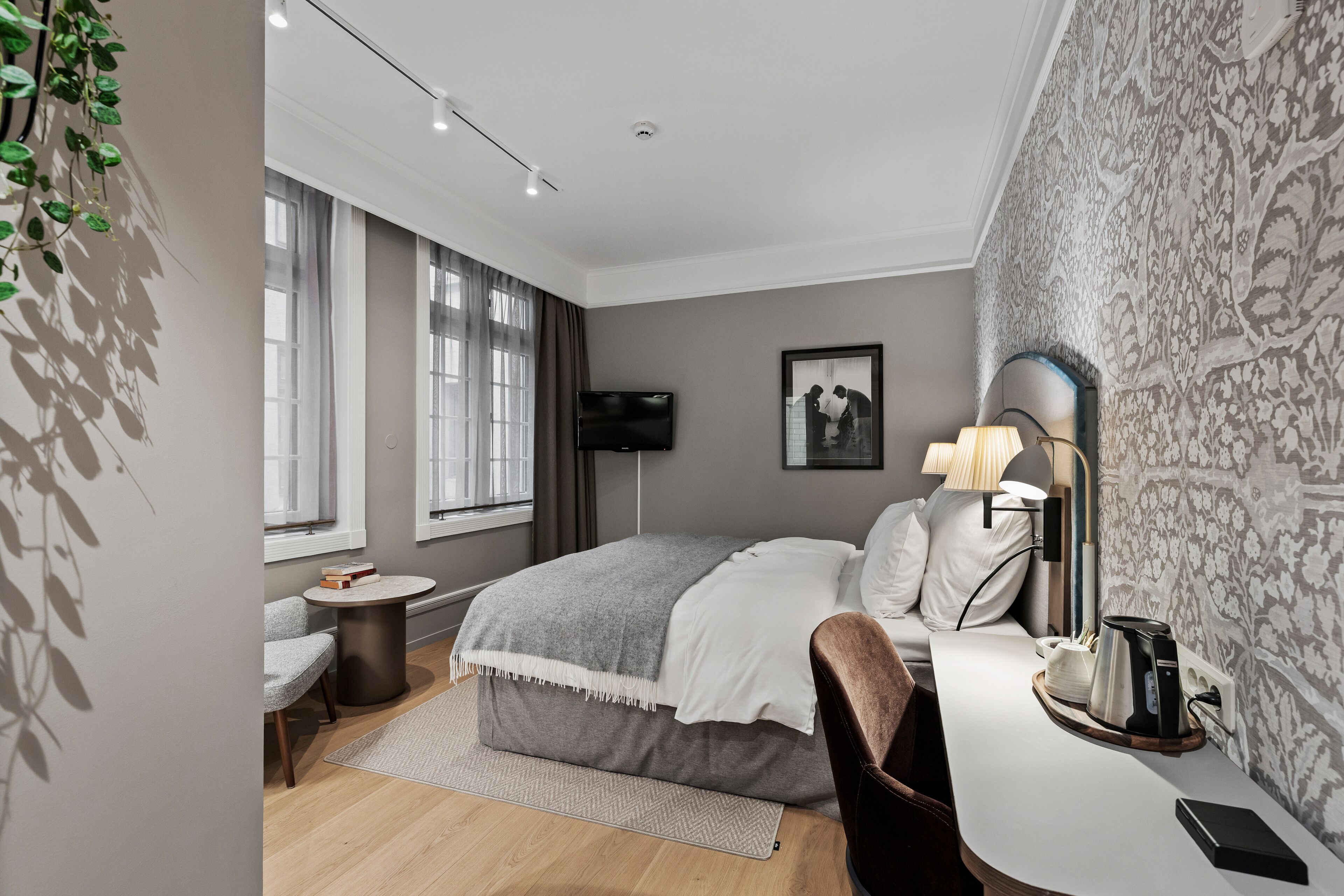 Un dormitorio moderno con cama, mesita de noche, lámpara y una pequeña mesa redonda con una silla.