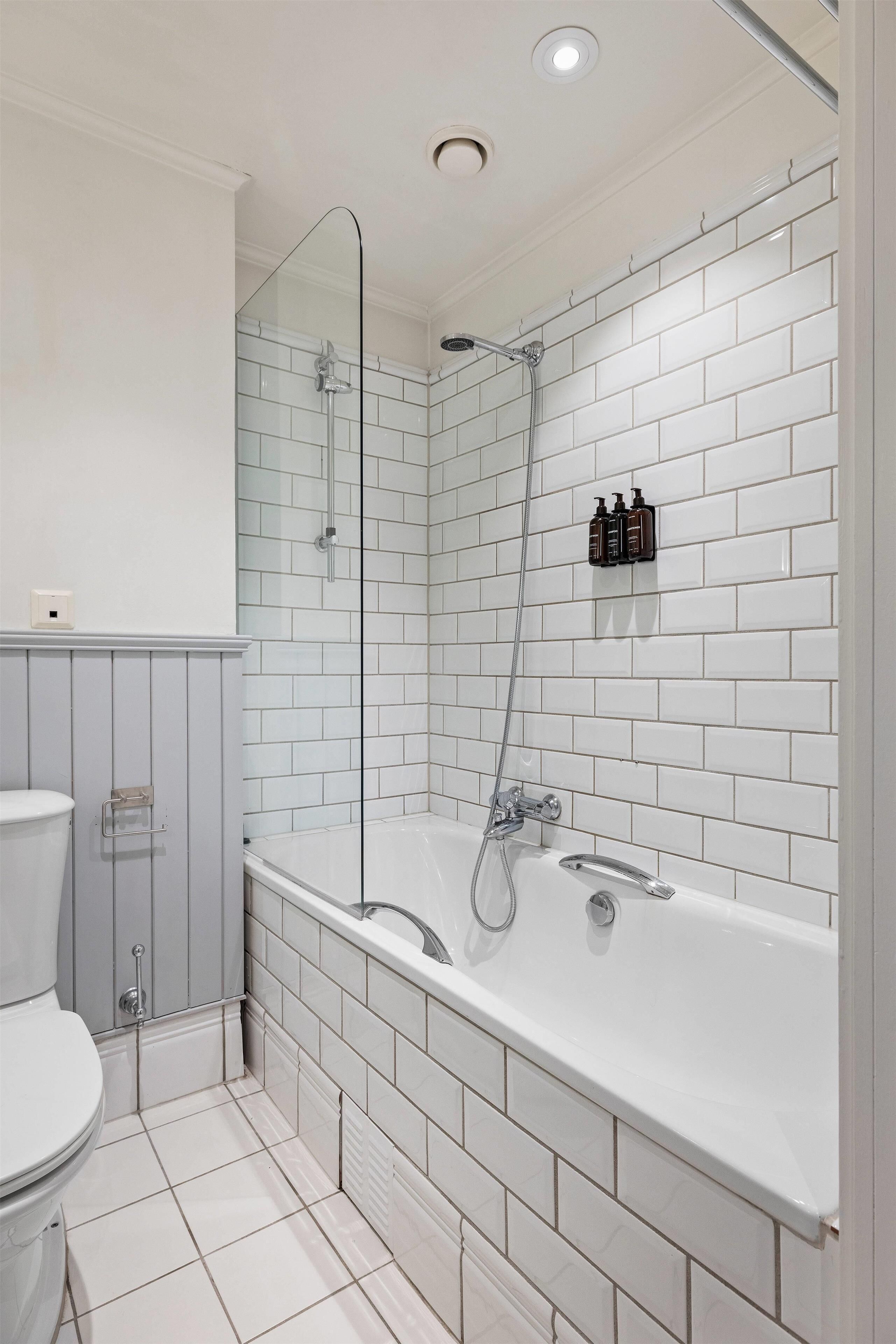 Un baño con una bañera blanca, ducha con mampara de vidrio y un inodoro.