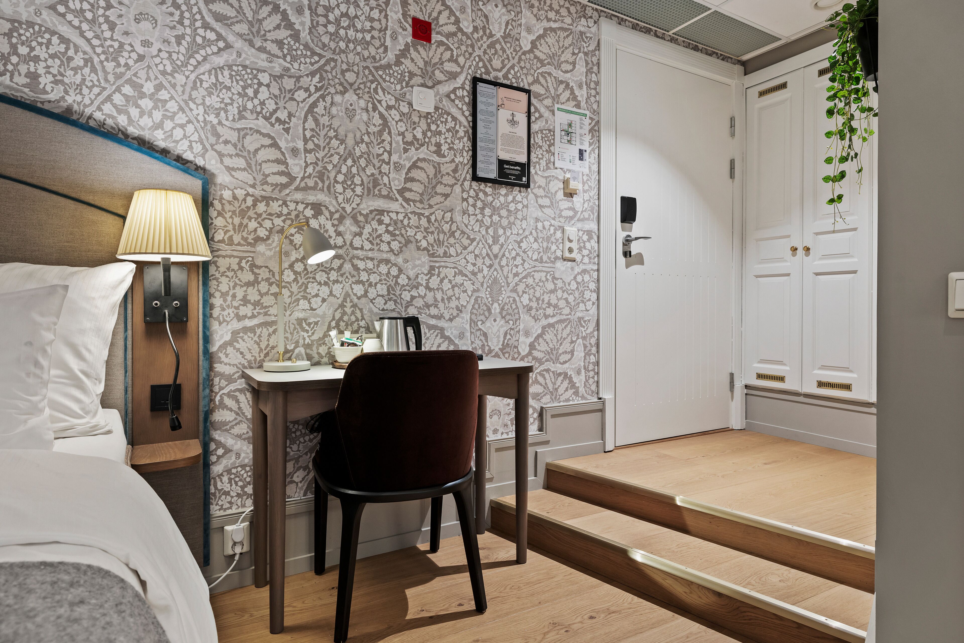 A hotel room with a bed, desk, chair, lamp, and a staircase leading to a door.
