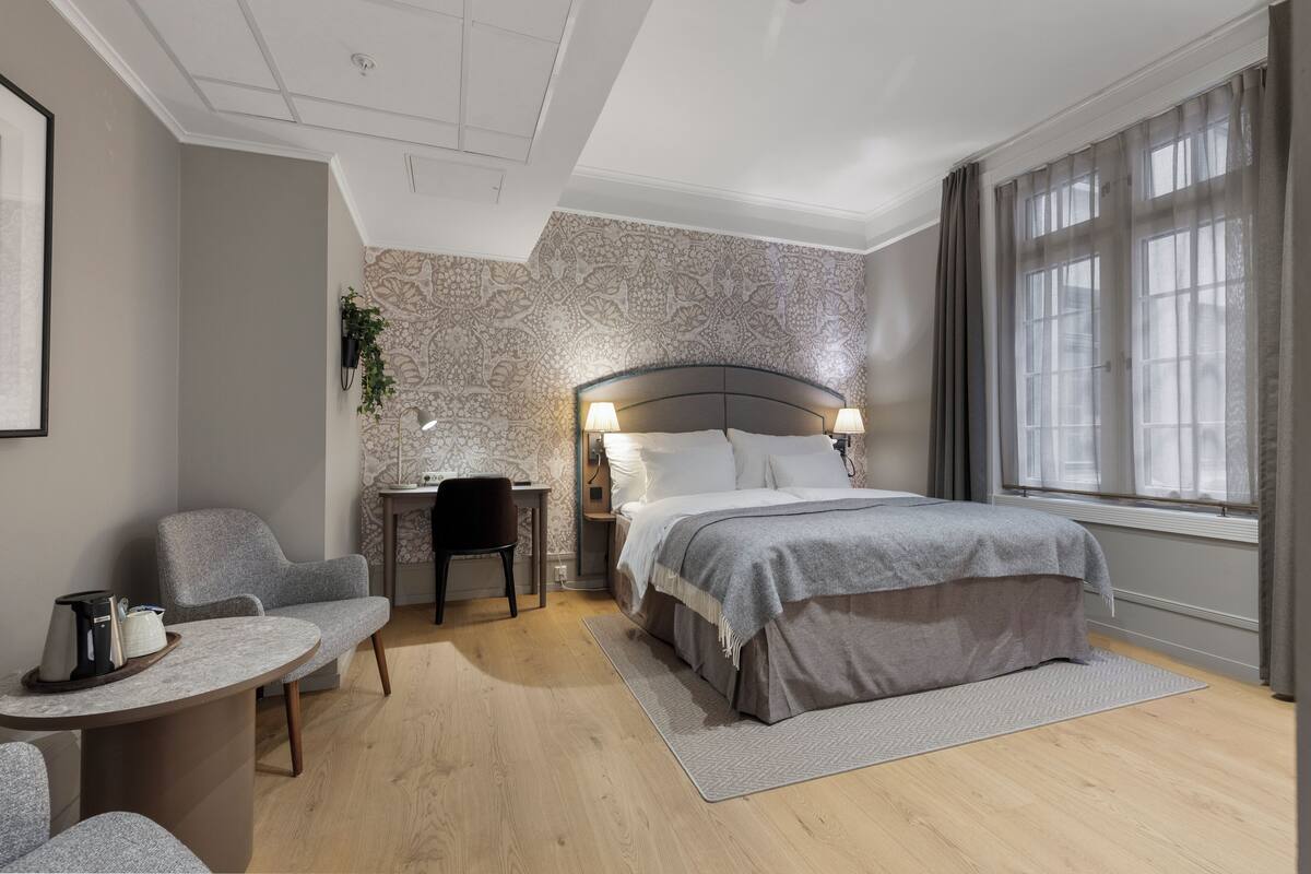 Un dormitorio con cama, mesita de noche, silla y un pequeño escritorio.