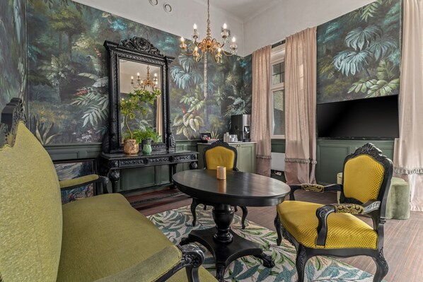 Ein Zimmer mit einem runden Tisch, zwei Stühlen, einem großen Spiegel und einer Kristallleuchter.