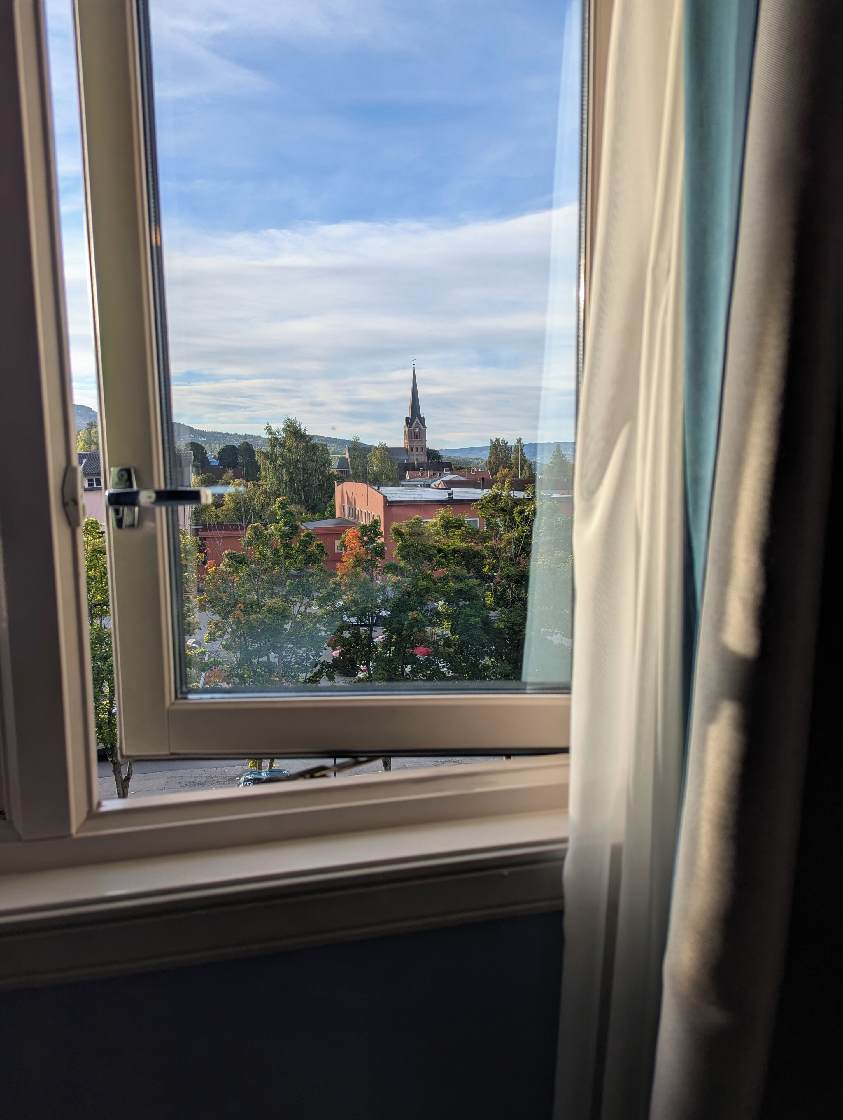 A window with a view of a church steeple and surrounding buildings.