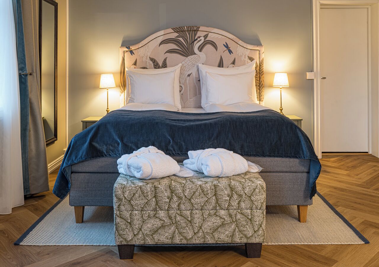 A bedroom with a bed, two bedside lamps, a bench, and a patterned rug.