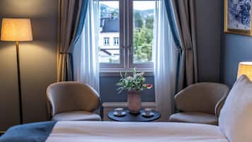A hotel room with a bed, two chairs, a small table with a vase of flowers, and a window with curtains.