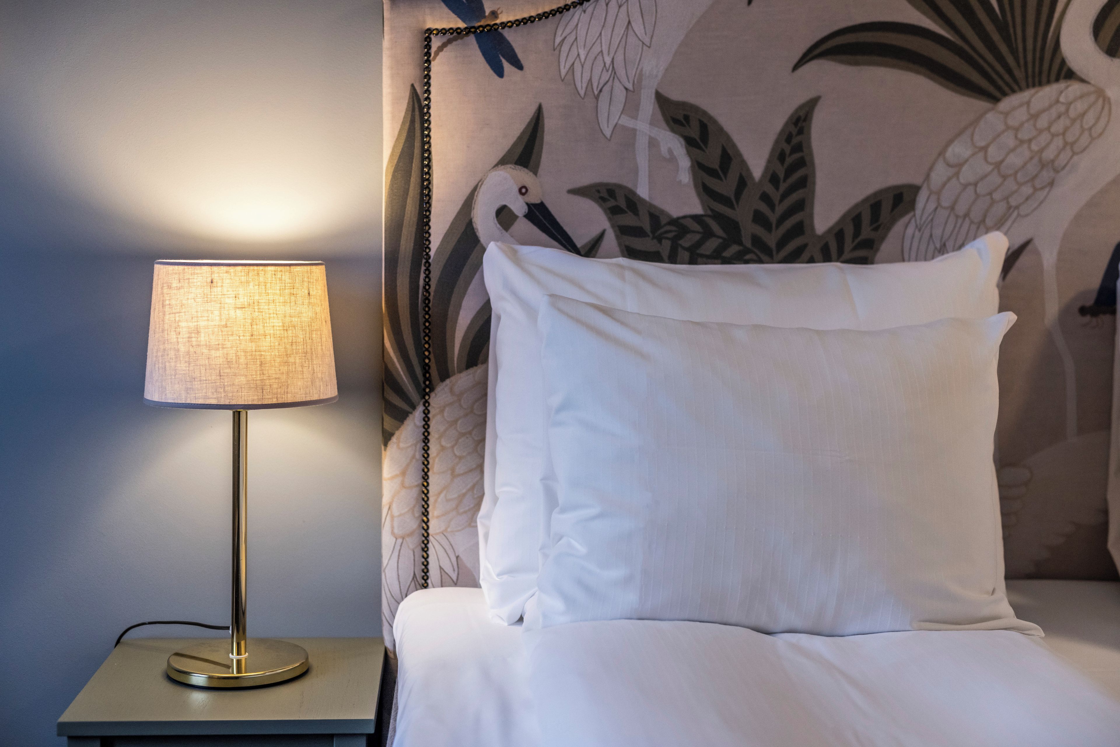 A bed with white bedding, a lamp on a bedside table, and a wall with a tropical leaf pattern.