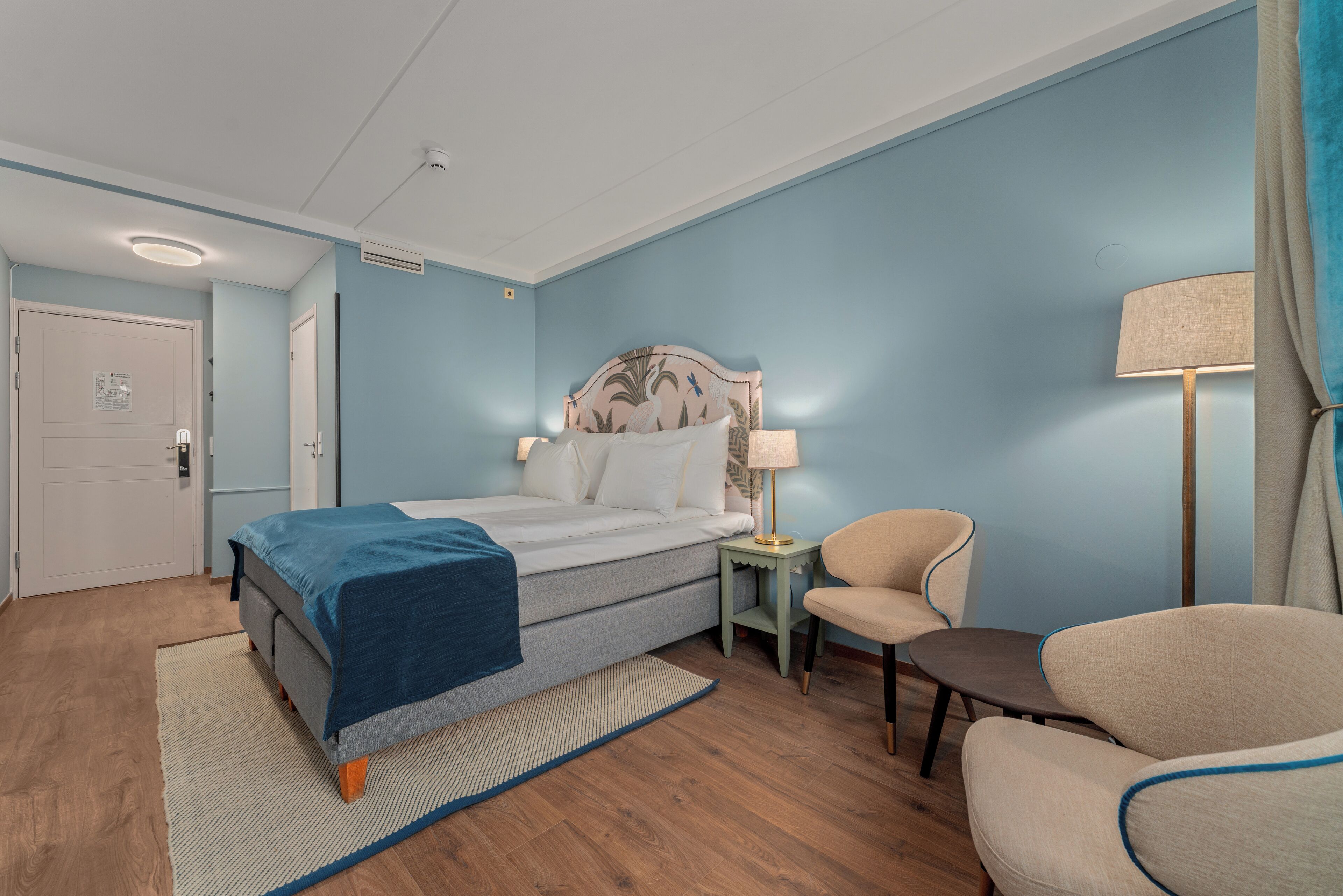 A bedroom with a bed, a chair, a nightstand, and a lamp.