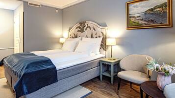 Un dormitorio ordenado con cama, lámparas de noche, una silla y una mesita con un jarrón de flores.