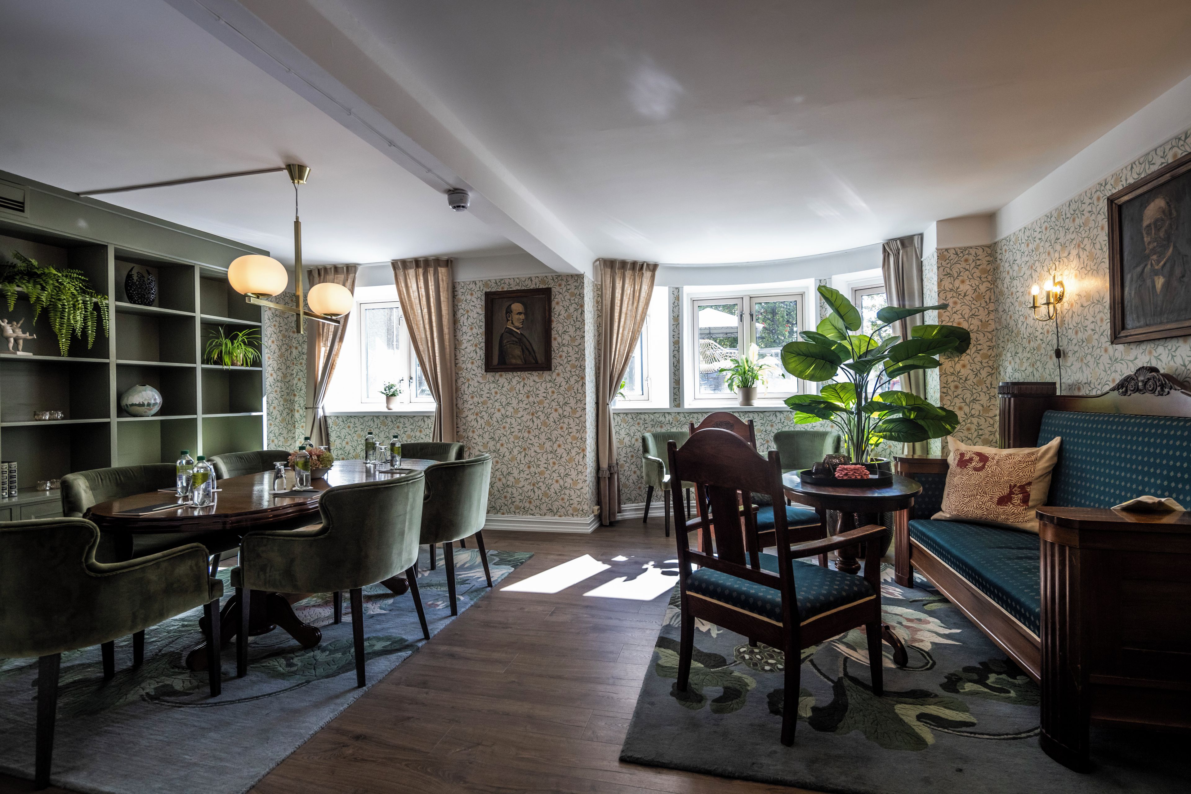 A room with a dining table, chairs, a sofa, a bookshelf, and a large plant.