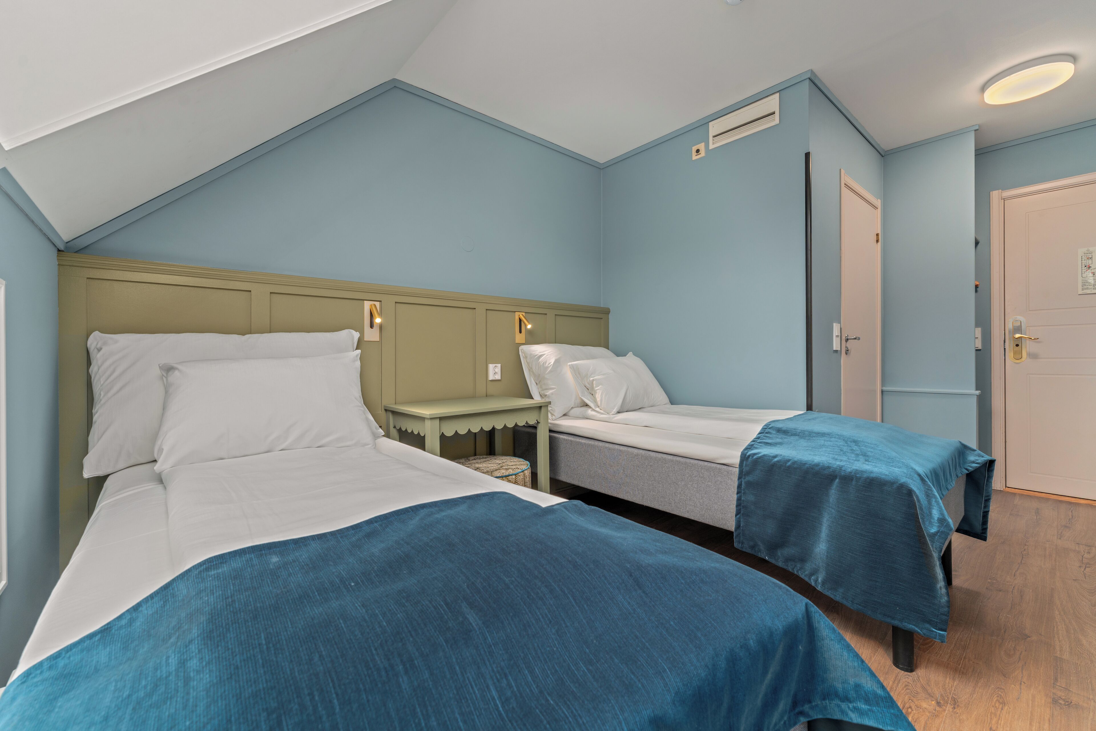 A bedroom with two beds, a small bedside table, a door, and a ceiling light.
